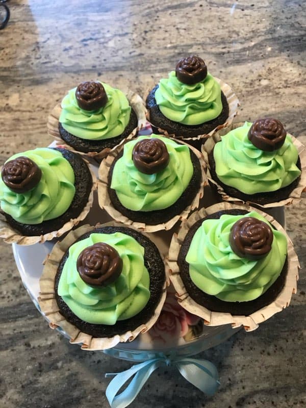 A plate of chocolate cupcakes topped with green frosting and a chocolate candy rose.