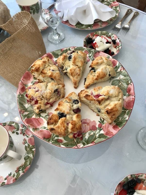 A floral plate holds several scones accompanied by a small dish of berries and yogurt.