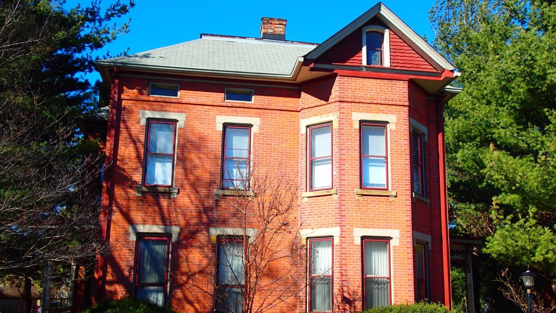 A red brick Victorian house surrounded by trees and greenery.