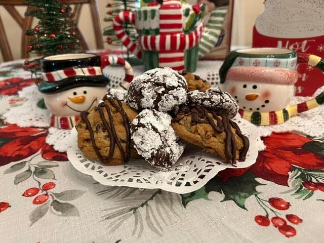 A plate of assorted festive cookies surrounded by cheerful snowman mugs and holiday decor.