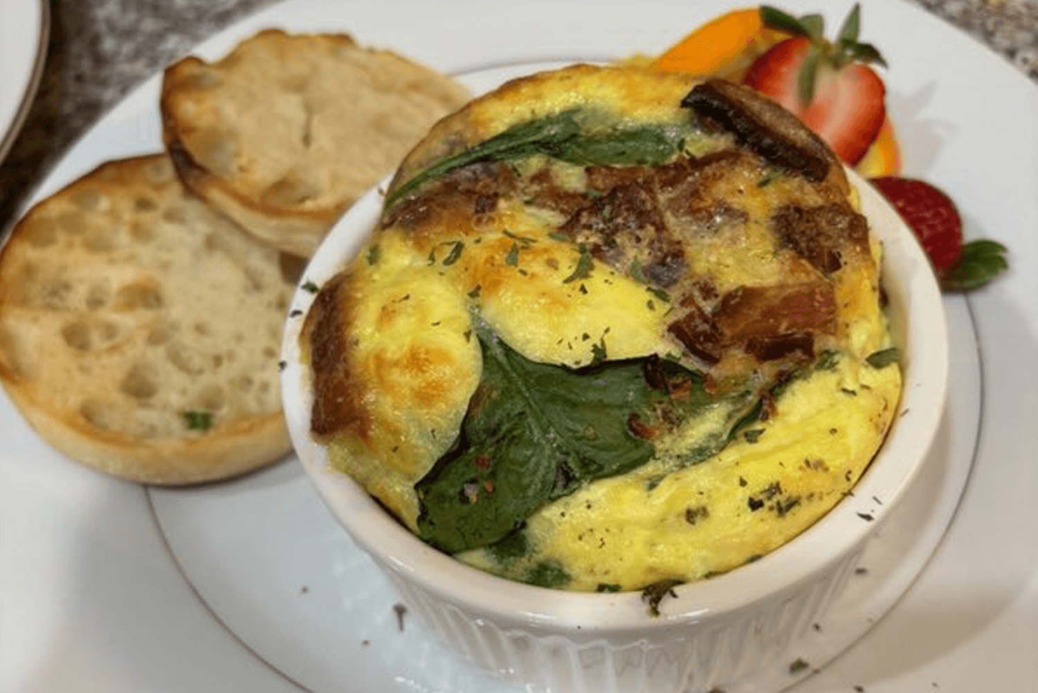 A baked spinach and bacon egg dish served with toasted bread and fresh fruit.