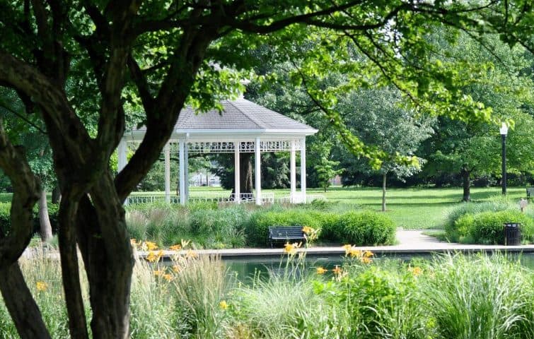 A white gazebo surrounded by lush greenery and flowers in a park.