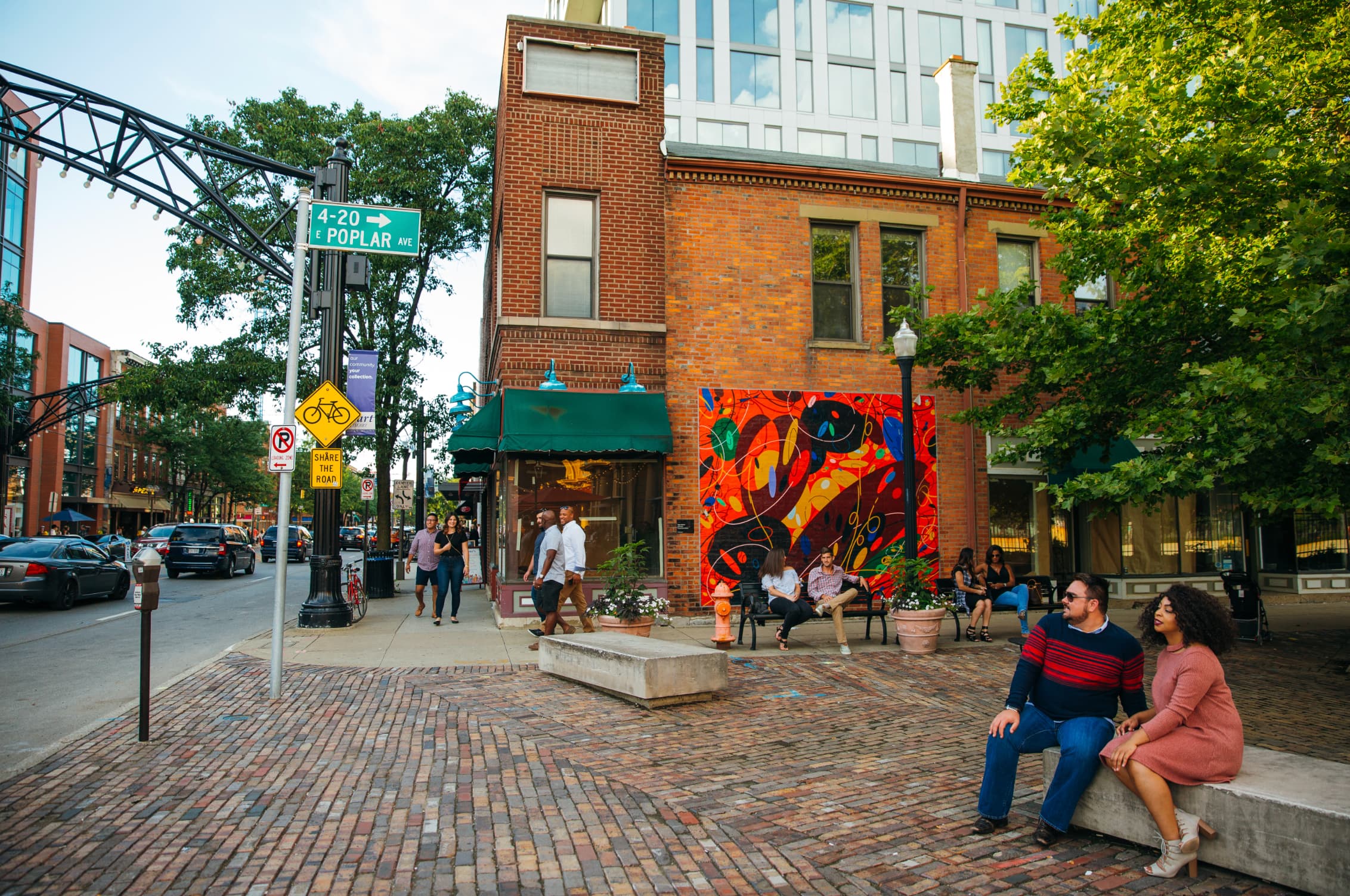 exterior shot of downtown with brick sidewalks.  Couples walking and setting on park benches shaded by the trees exterior shot of downtown with brick sidewalks.  Couples walking and setting on park benches shaded by the trees